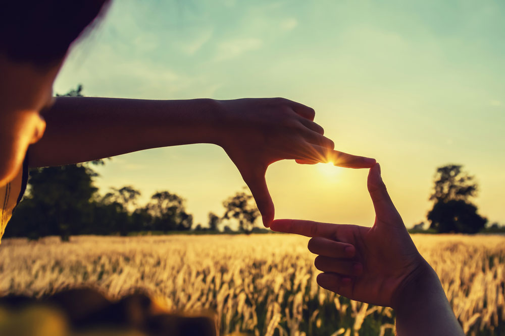 Fingers forming frame for sunset image over fields